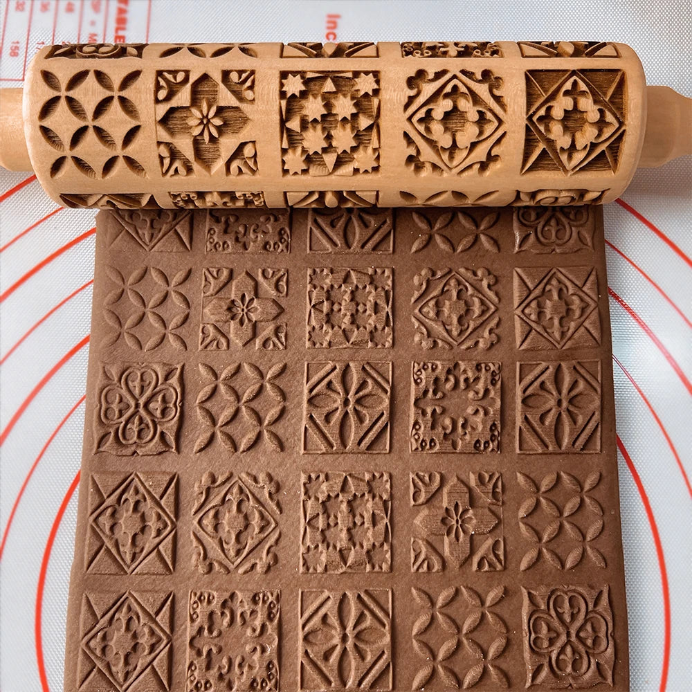Embossed rolling pin with intricate geometric patterns presses into brown dough on a pastry mat, creating a decorative design of squares and diamonds.