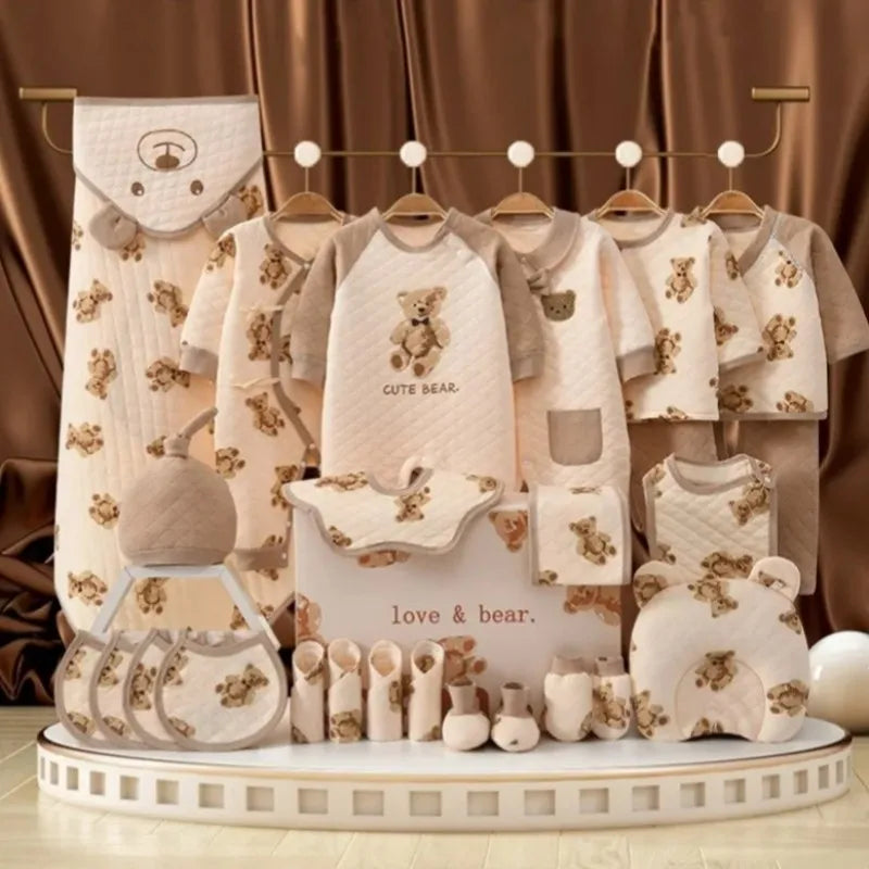 Baby clothing set with teddy bear designs, including onesies, bibs, socks, and caps in beige and white. Displayed on hangers and a stand with a "love & bear" sign.