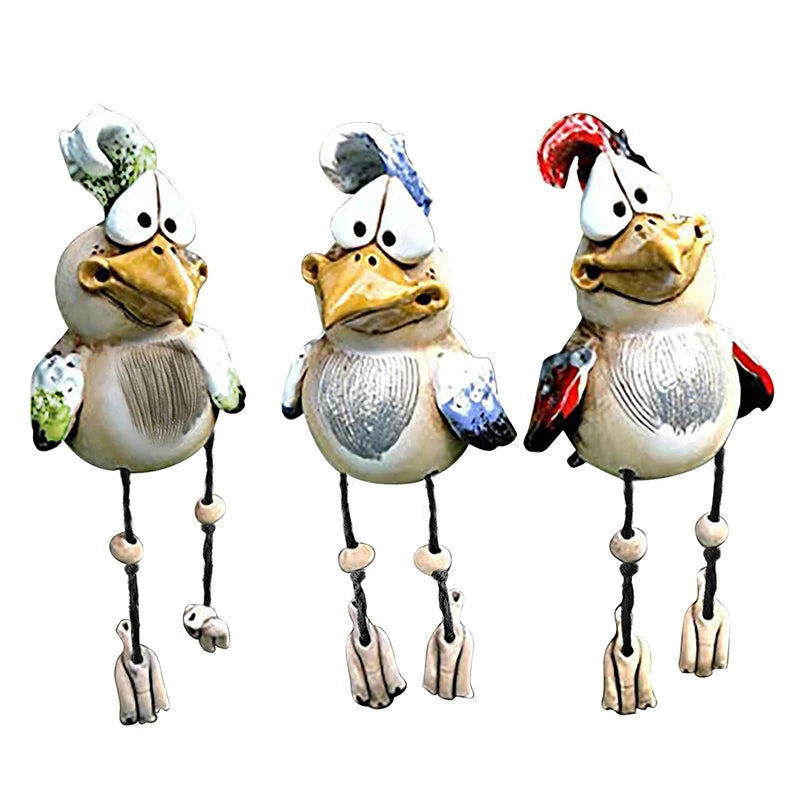 Three whimsical ceramic bird sculptures with exaggerated features, long legs, and vibrant crest colors (green, blue, red) are standing side by side against a white background.