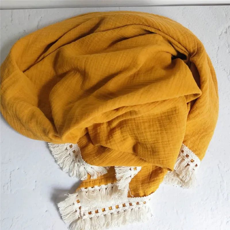 A mustard yellow scarf with white fringe tassels lies crumpled on a light surface, showcasing a textured fabric and decorative edging.