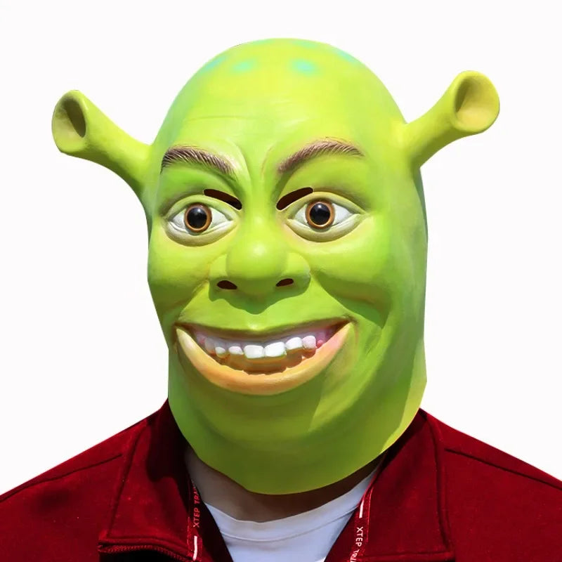 Person wearing a green ogre mask featuring large ears and a wide grin, dressed in a red jacket against a plain white background.