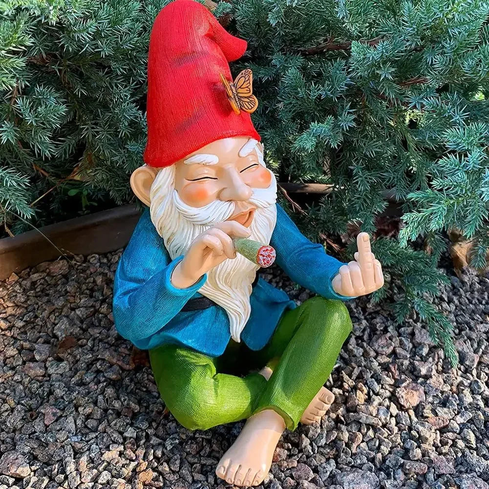 A garden gnome with a red hat and a butterfly, sitting on gravel, holds a smoking item and makes a playful gesture, surrounded by green foliage.
