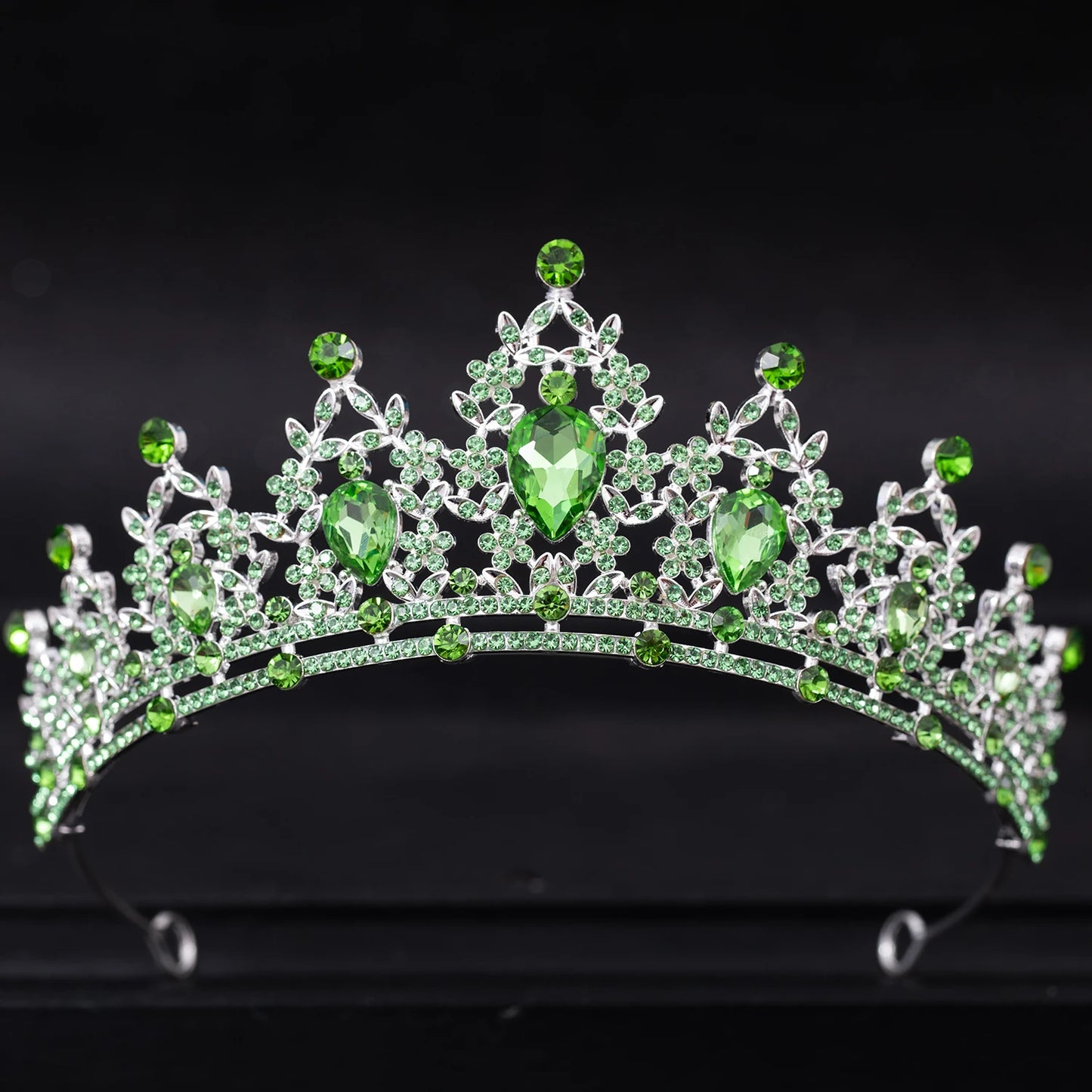 A silver tiara adorned with large green teardrop gemstones and smaller round gems, arranged in intricate patterns against a black background.