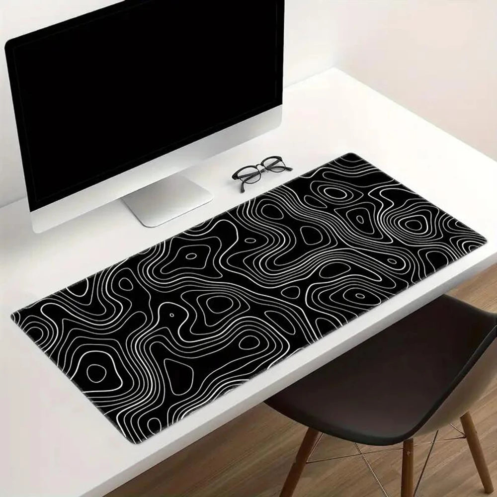 A minimalist workspace with a computer, glasses, and a large black desk mat featuring a white, abstract swirling line pattern, on a white desk beside a dark chair.
