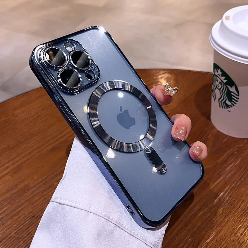A person holds a blue iPhone with a metallic ring attachment on the back, near a wooden table with a white Starbucks cup. The phone's camera features three lenses.