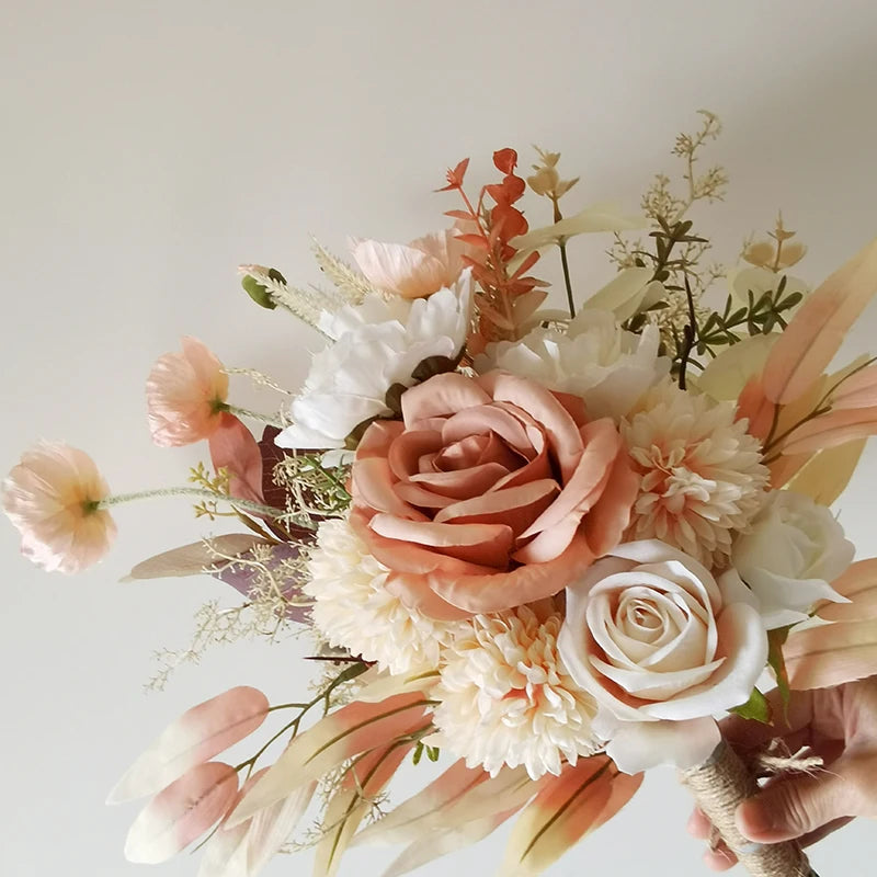 A bouquet of soft peach and white flowers, including roses and chrysanthemums, with green and beige foliage, held against a light background.
