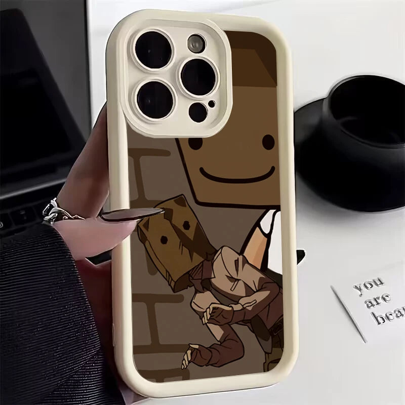 Smartphone case featuring a cartoon design of two characters with paper bag masks, one smiling. A hand with black nails holds the phone, with a desk in the background.