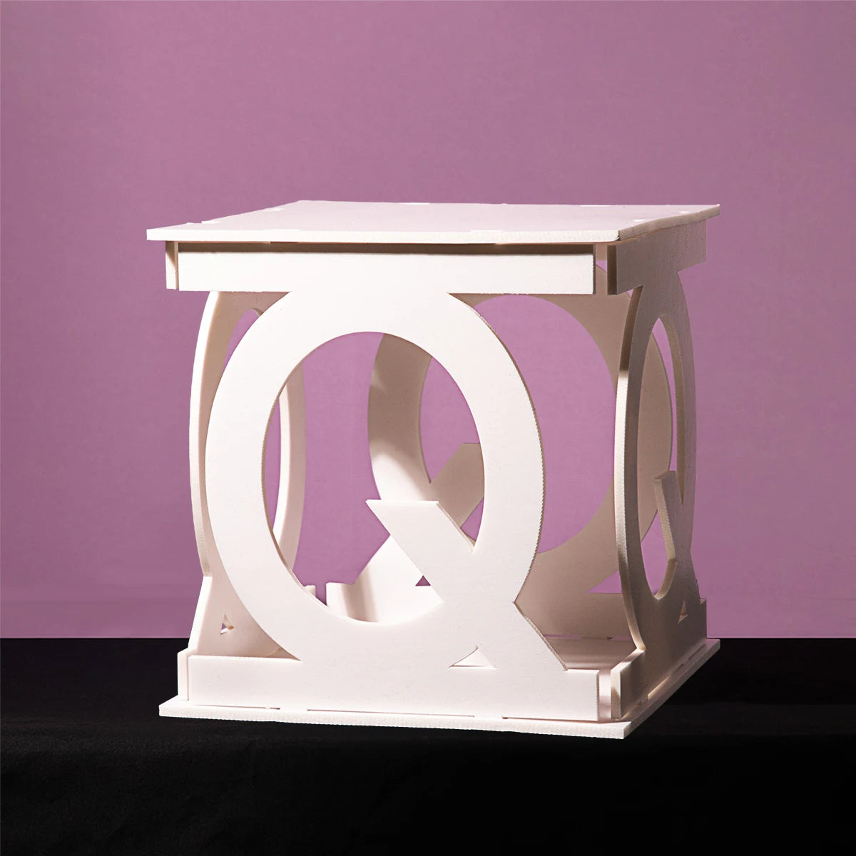 White cube-shaped table with circular cutouts on each side, placed on a black surface against a purple background.