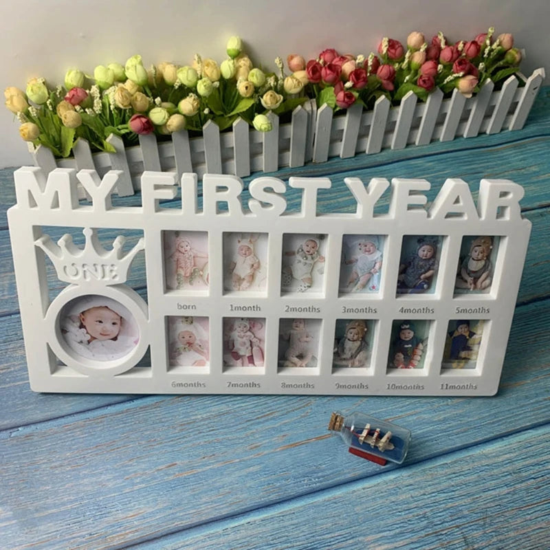 A photo collage frame labeled "My First Year" shows monthly baby pictures from birth to 11 months. A small ship in a bottle and flowers are arranged on a blue wooden surface.
