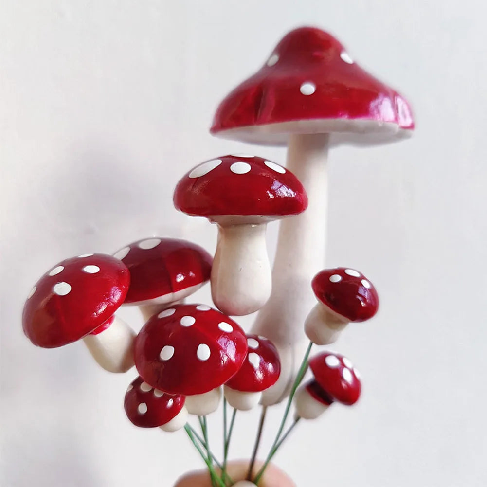 A cluster of red and white spotted mushrooms with glossy caps and stems. The mushrooms vary in size, with the largest one towering above the rest against a plain background.