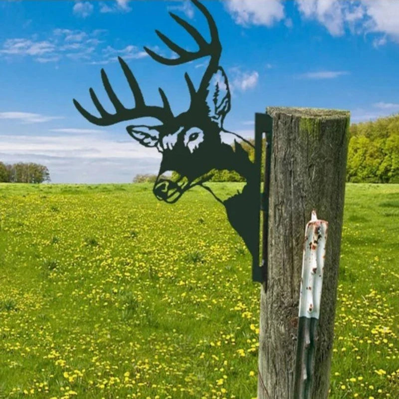 Metal deer silhouette protruding from a wooden post in a grassy field with yellow flowers under a blue sky.