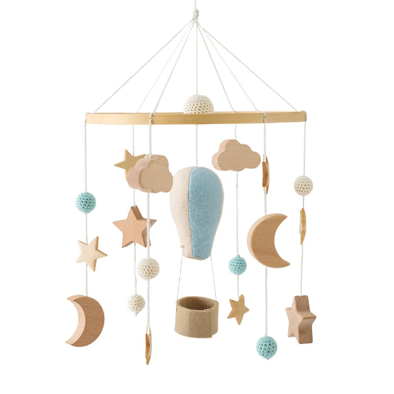 Wooden baby mobile featuring a hot air balloon, stars, clouds, moons, and crocheted balls in soft colors, suspended from a wooden ring.