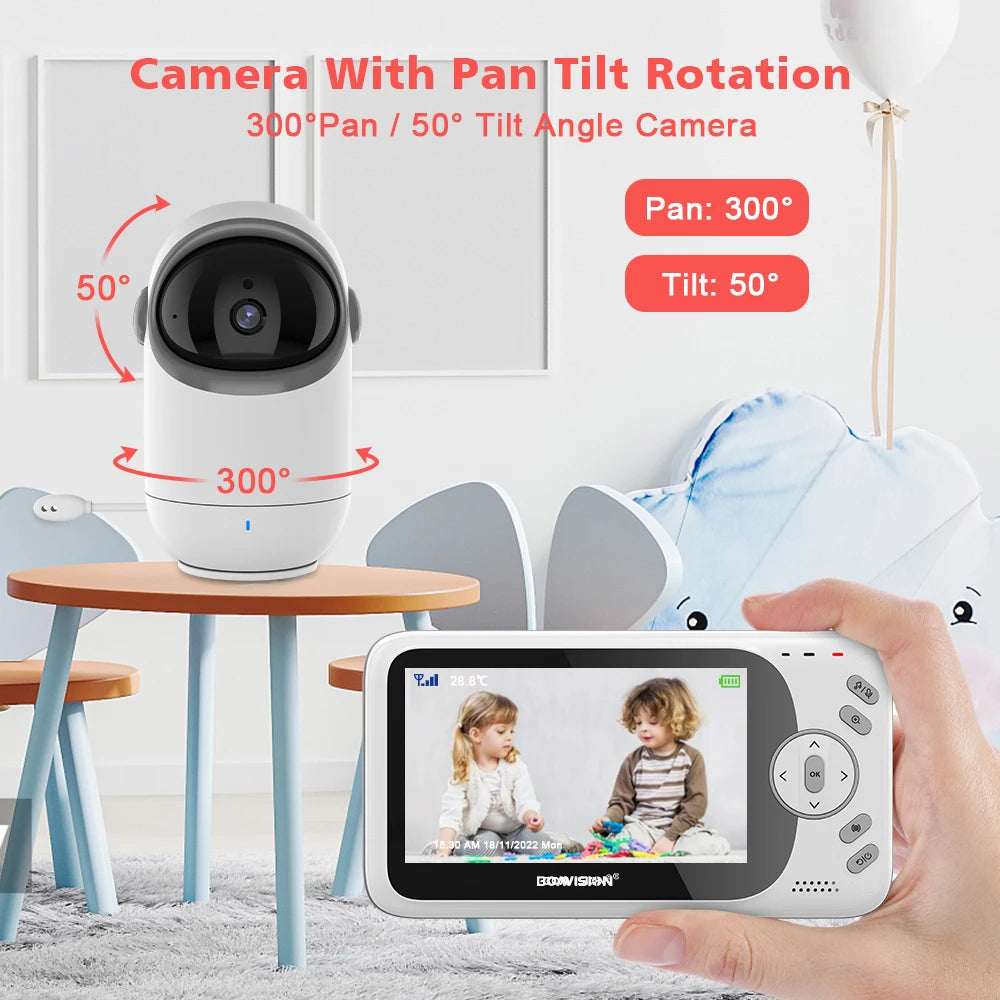 Smart camera with 300° pan and 50° tilt capability on a table. Hand holds monitor displaying two children playing, set in a cozy room with chairs and a soft toy.
