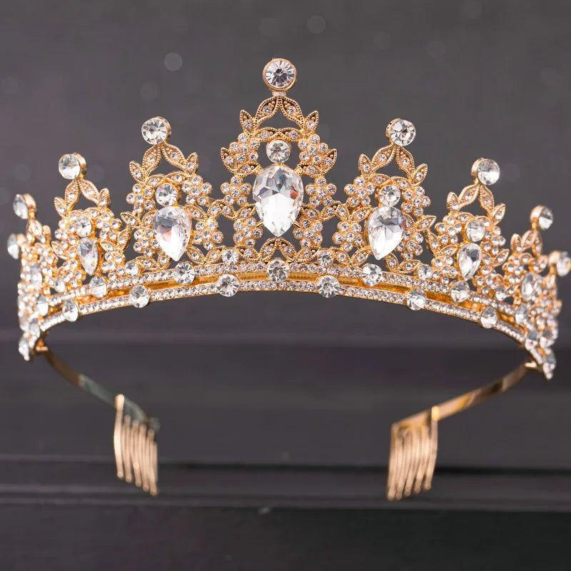 A golden tiara adorned with large teardrop-shaped and circular crystals on a dark background, featuring intricate detailing and attached combs for securing to the hair.