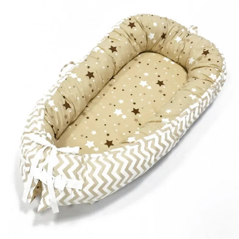 Cozy baby lounger with a beige base featuring brown and white stars, surrounded by a chevron-patterned padded border. Tied with white ribbons at the end.