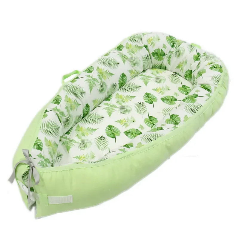 Cozy baby lounger with a light green exterior and a leafy pattern on the inside, resembling various tropical leaves, complete with a bow and strap on one end.