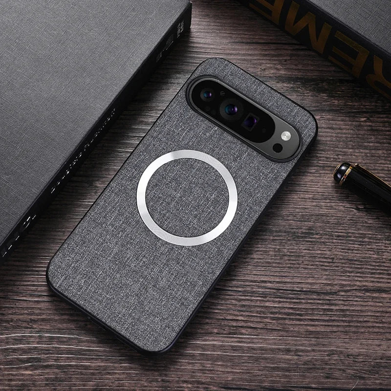 A smartphone with a dark fabric-textured case featuring a silver ring on the back is placed on a wooden surface beside a book and a pen.