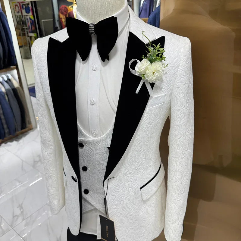 Mannequin dressed in an ornate white suit with black lapels, a matching vest, and a black bow tie. A white boutonniere adorns the left lapel.