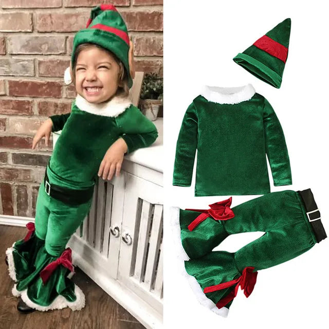 A young child smiles, dressed as a Christmas elf in a green costume with a hat, red ribbons, and faux fur trim. The outfit is shown separately on the right.