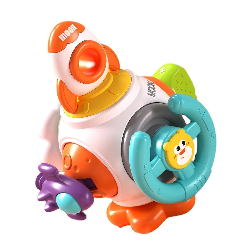 Colorful toy spaceship with a launch pad base, orange and white rocket, teal steering wheel with a monkey face, and a small purple plane feature.
