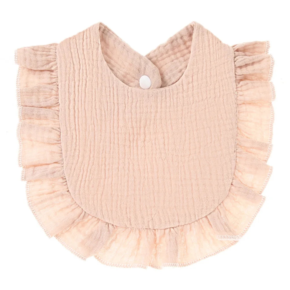 A soft pink baby bib with a textured fabric, featuring ruffled edges and a snap closure at the neck.