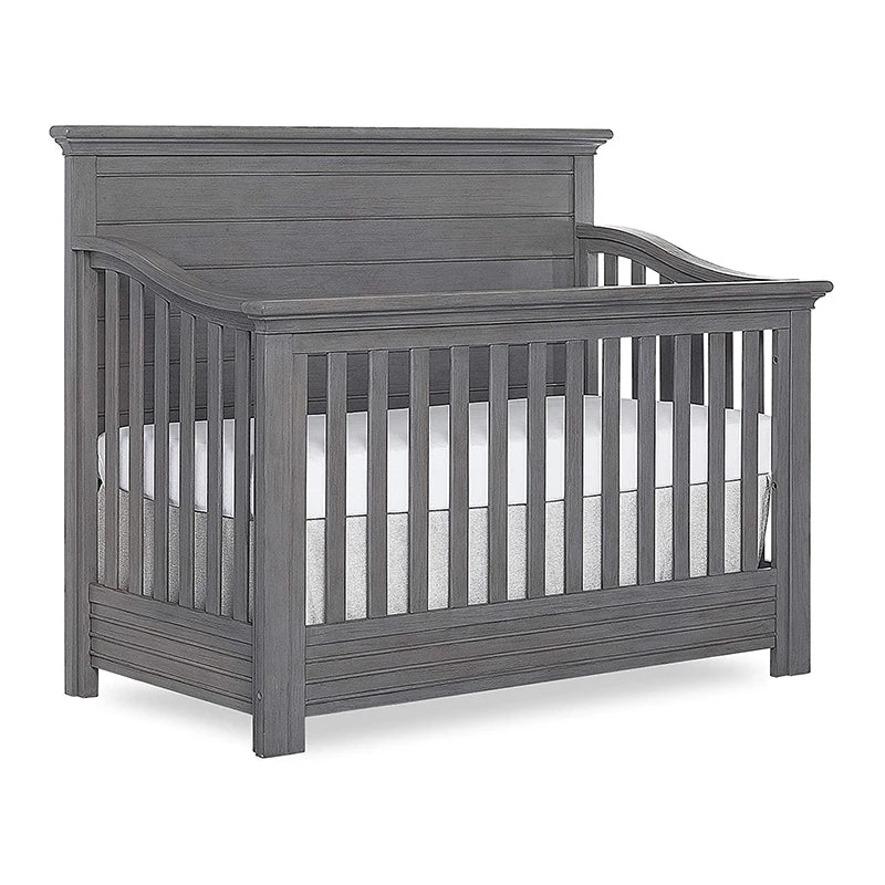 Gray wooden baby crib with vertical slats and an arched headboard, featuring a white mattress. The design is classic and sturdy, suitable for a nursery.