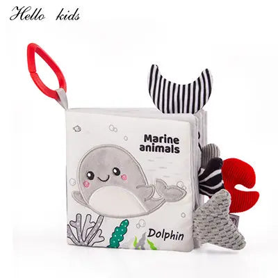 Soft baby book titled "Marine Animals" with a dolphin illustration. Features colorful fabric tail and claw tabs, and a red handle. Designed for tactile engagement.