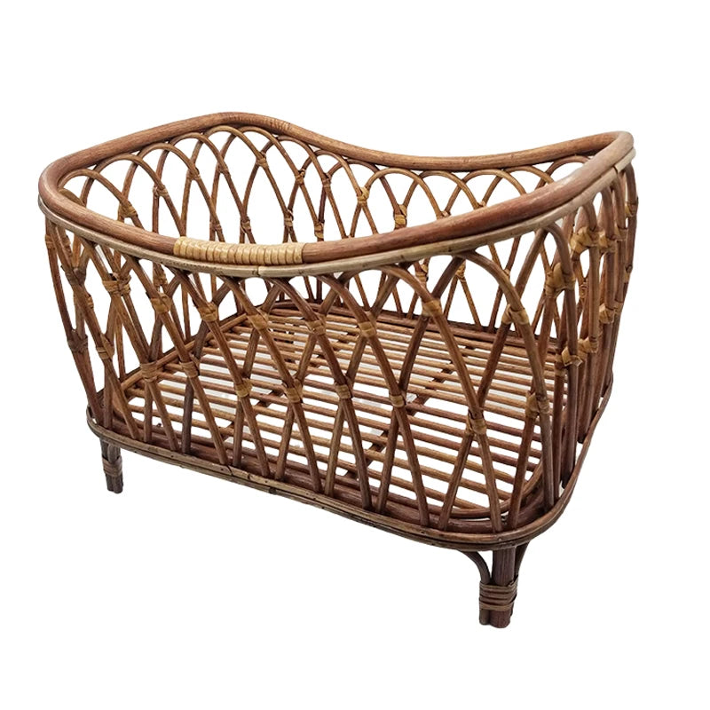 Rattan baby bassinet with an open weave design, featuring a natural brown finish. The bassinet has a slatted base and stands on four sturdy legs.
