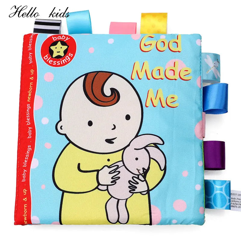 Soft baby book titled "God Made Me" with a cartoon baby holding a bunny on a blue background. Colorful ribbon tags line the edge for tactile play.