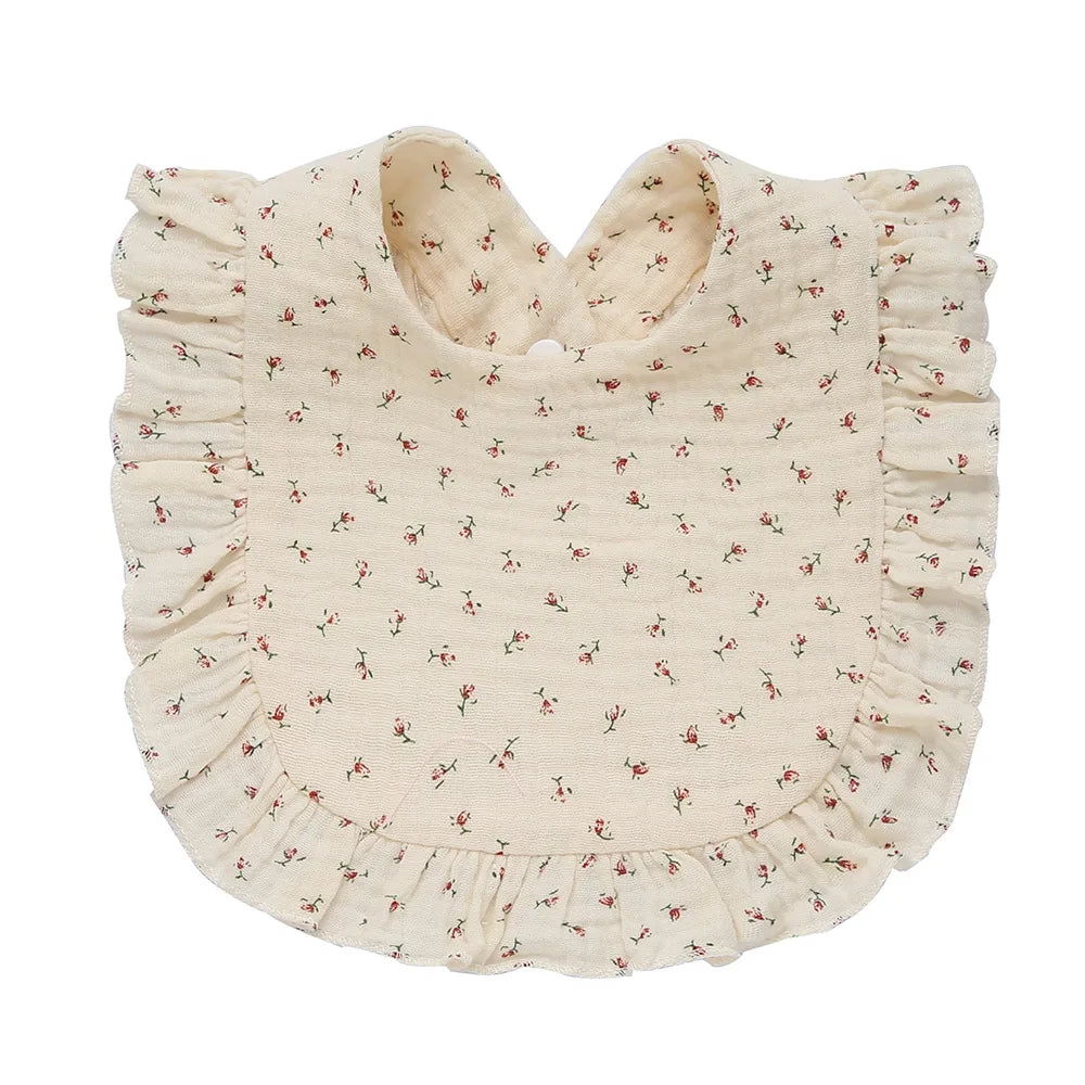 Cream-colored baby bib with a delicate pink floral pattern and ruffled edges. Fastened at the neck, the design is charming and suitable for a vintage-inspired style.