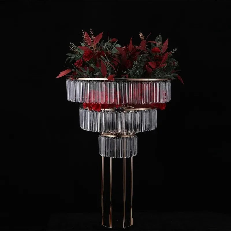 Elegant gold and glass stand adorned with lush red and green floral arrangement against a black background, creating a striking and sophisticated display.