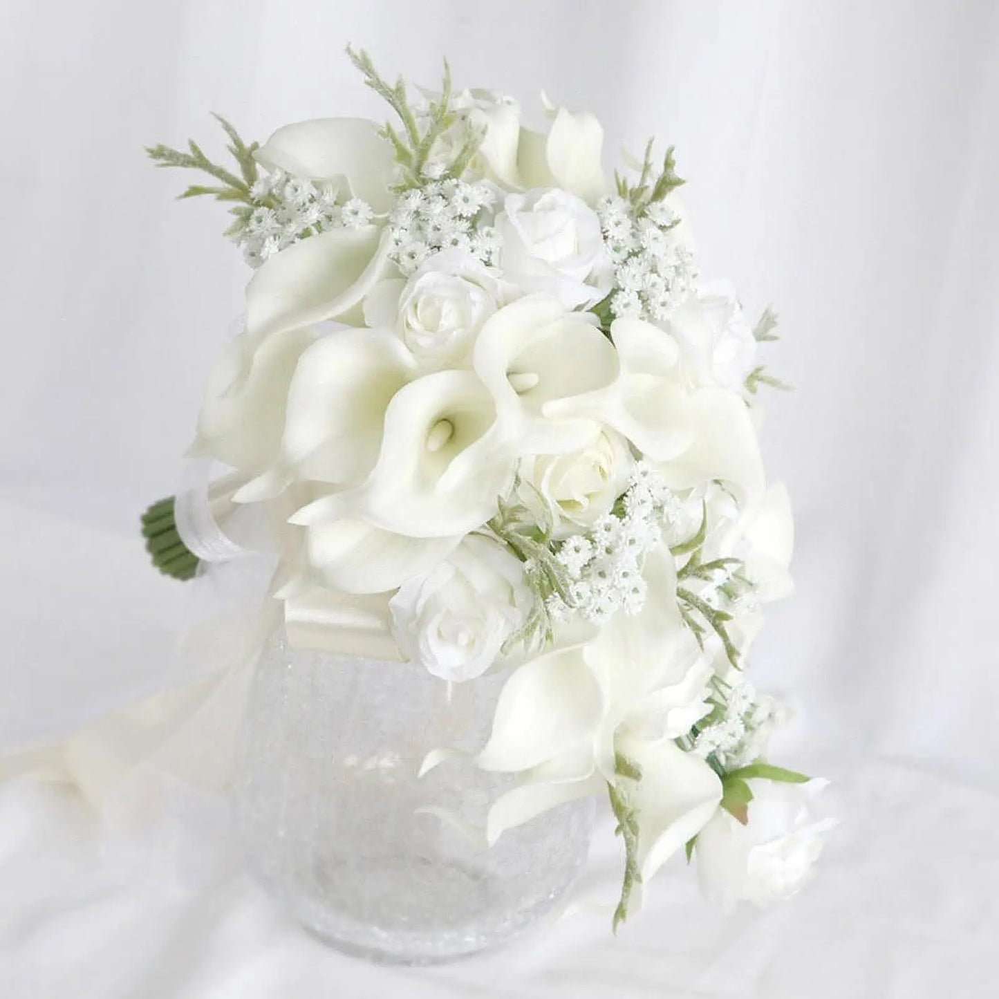 Elegant bouquet of white calla lilies, roses, and baby's breath arranged in a clear vase against a white background.