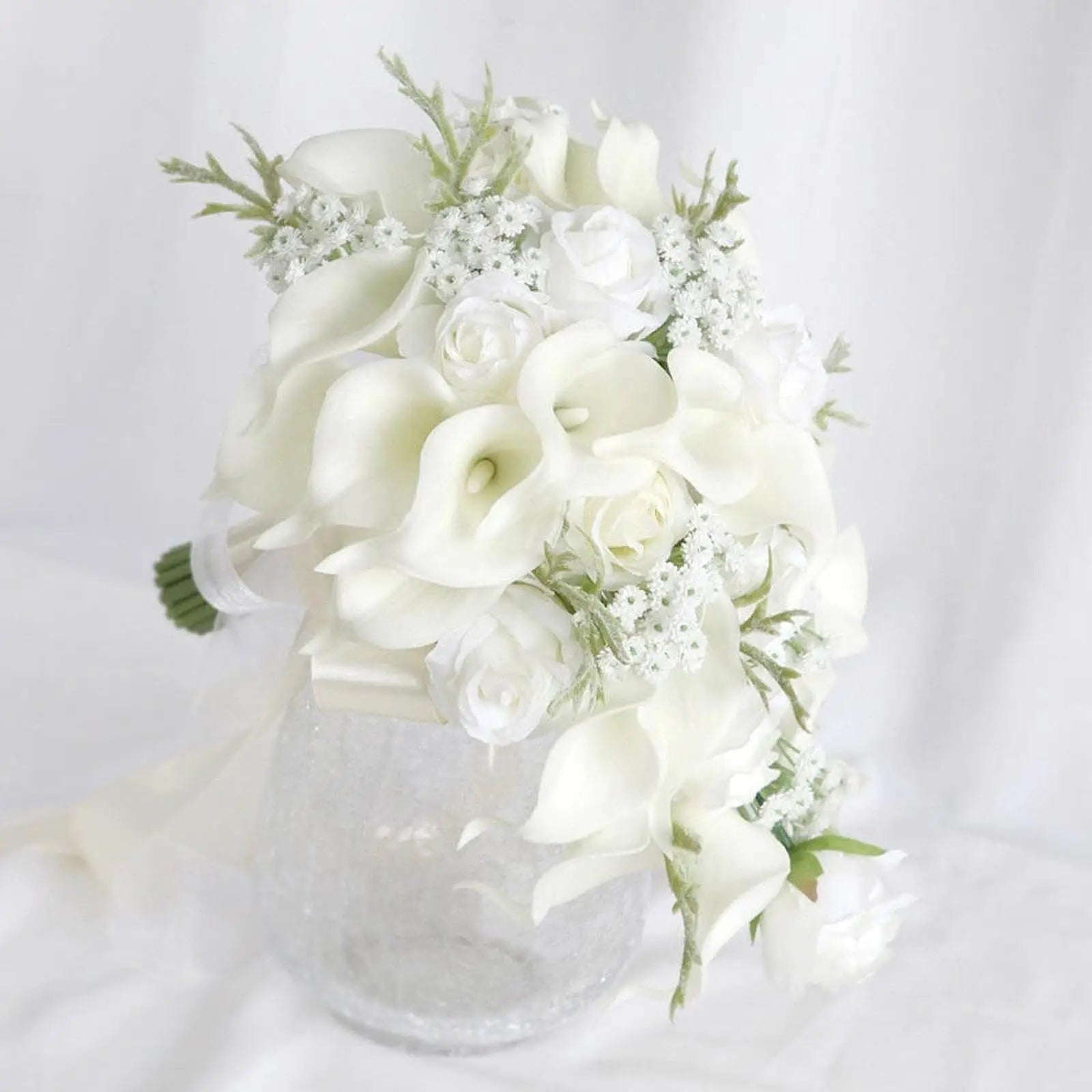 Elegant bouquet of white calla lilies, roses, and baby's breath arranged in a clear vase against a white background.