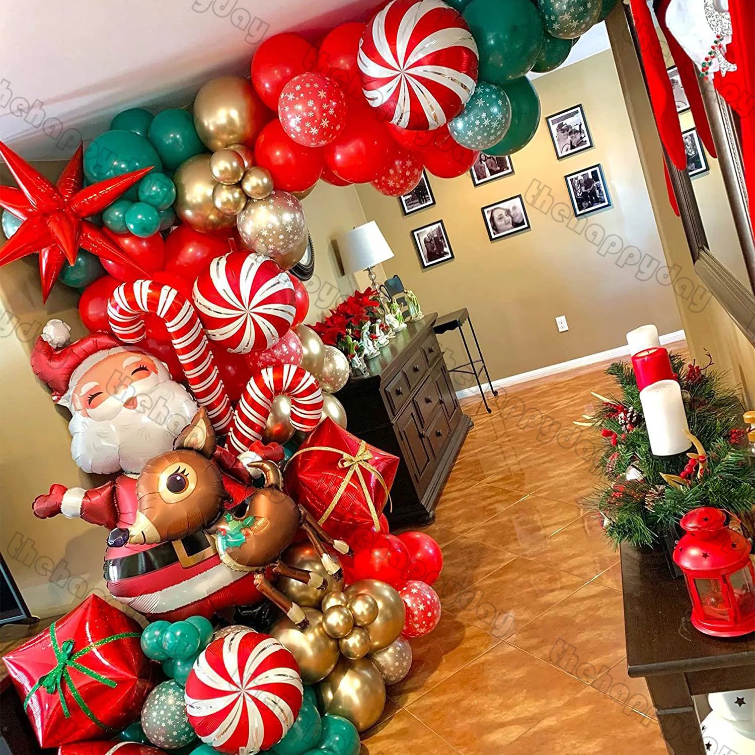 Festive hallway with a colorful balloon arch featuring Santa, reindeer, candy canes, red and gold ornaments. Red candles and greenery accent the console table.