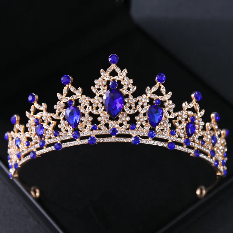 A golden tiara adorned with large pear-shaped blue gemstones and intricate designs of small clear stones, set against a dark background.