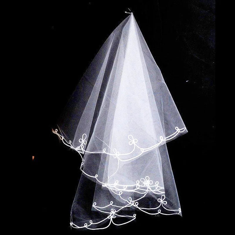 White wedding veil with scalloped edges and intricate floral embroidery, set against a dark background.