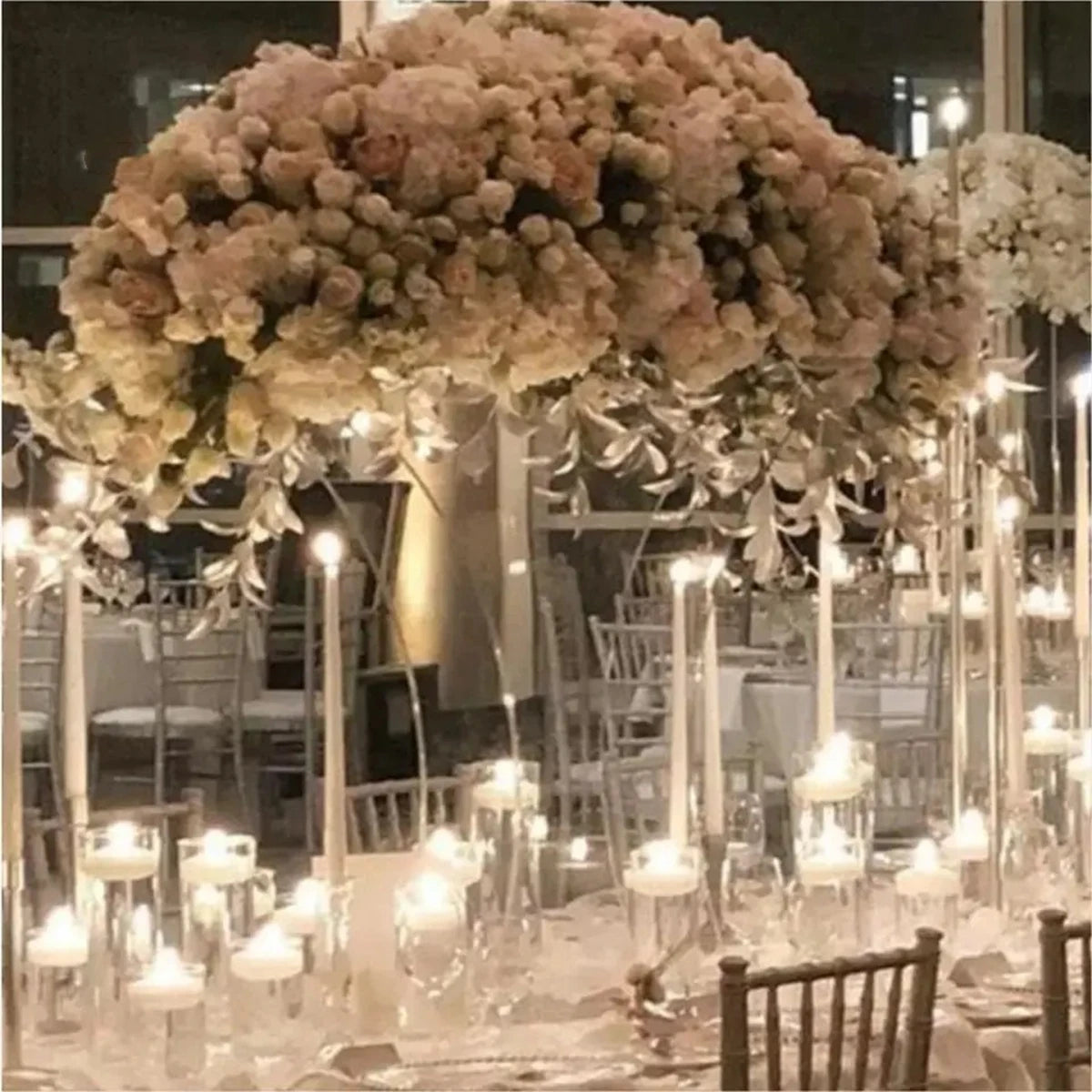 Elegant wedding reception with lavish floral centerpiece, glowing candles, and neatly arranged tables with white linens and clear chairs, creating a romantic, intimate ambiance.
