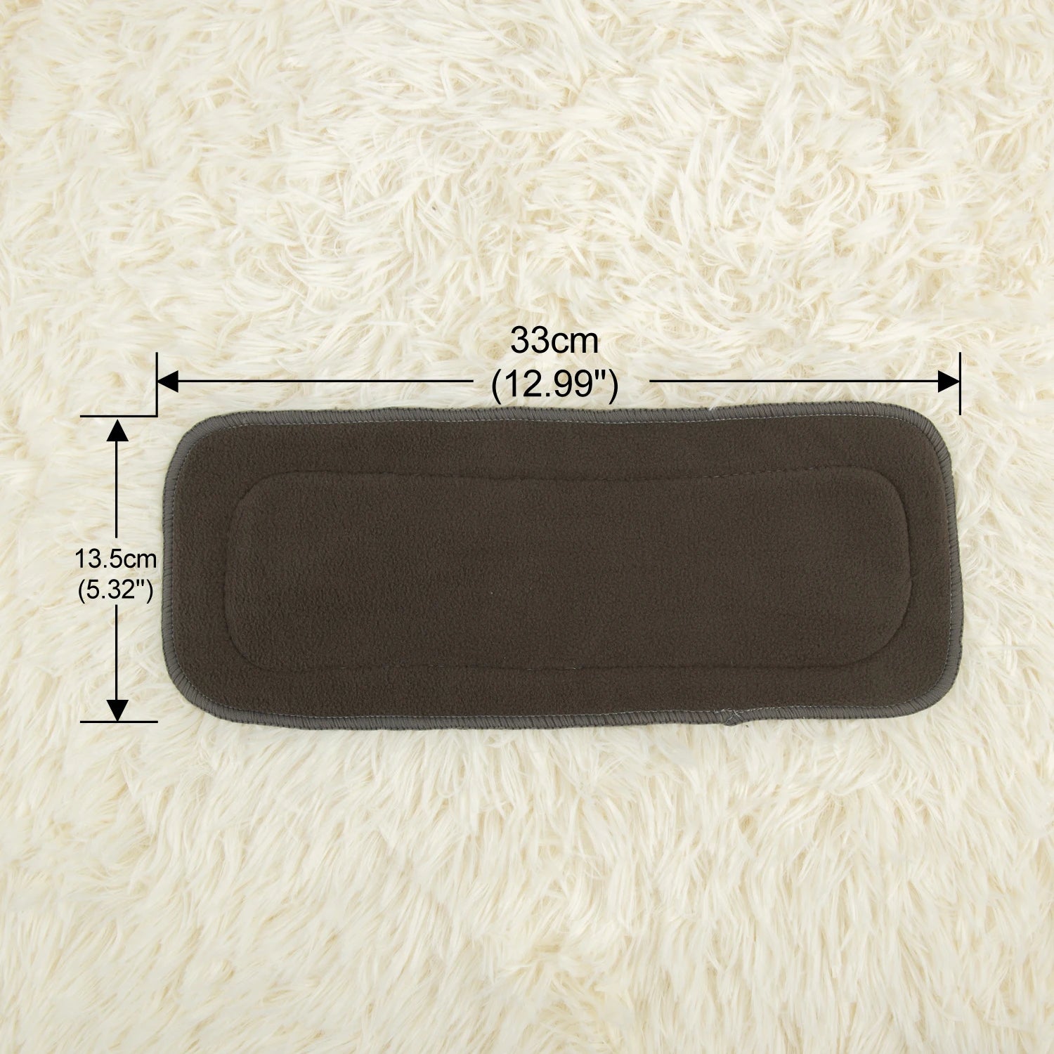 Dark gray rectangular pad measuring 33cm by 13.5cm placed on a fluffy white surface. Dimensions are labeled, indicating 12.99 inches by 5.32 inches.