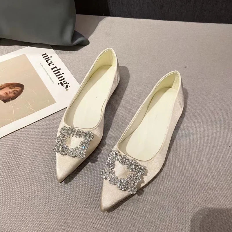Elegant cream-colored pointed flats with large rhinestone buckles, set on a gray surface next to an open magazine with a female portrait and text "nice things."