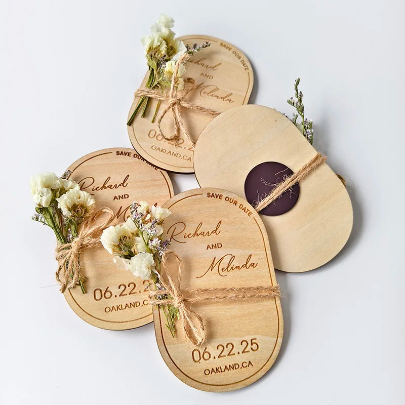 Wooden "Save the Date" magnets engraved with wedding details, decorated with tied white flowers and twine, displaying a June 22, 2025, wedding in Oakland, CA.
