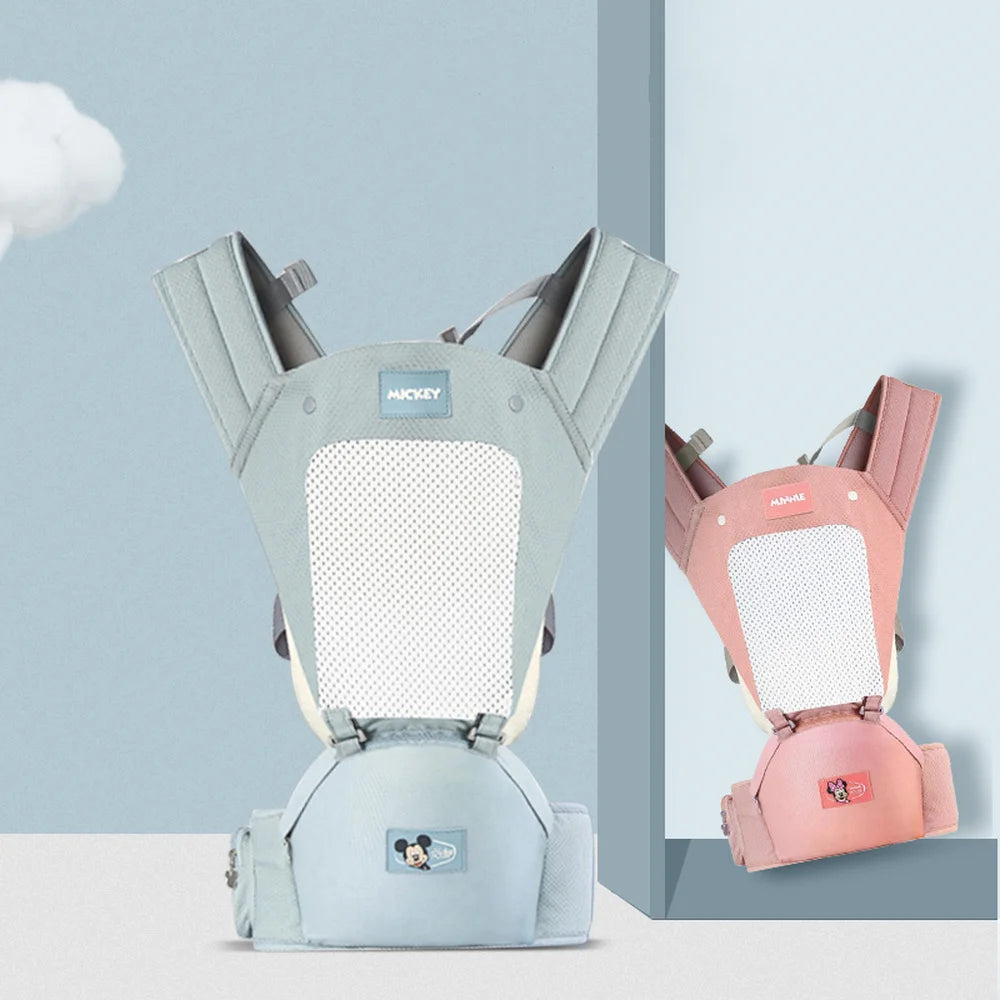Two baby carriers showcased side by side, one in light blue and the other in pink, both with mesh panels and Mickey Mouse-themed patches, set against a pastel blue background.