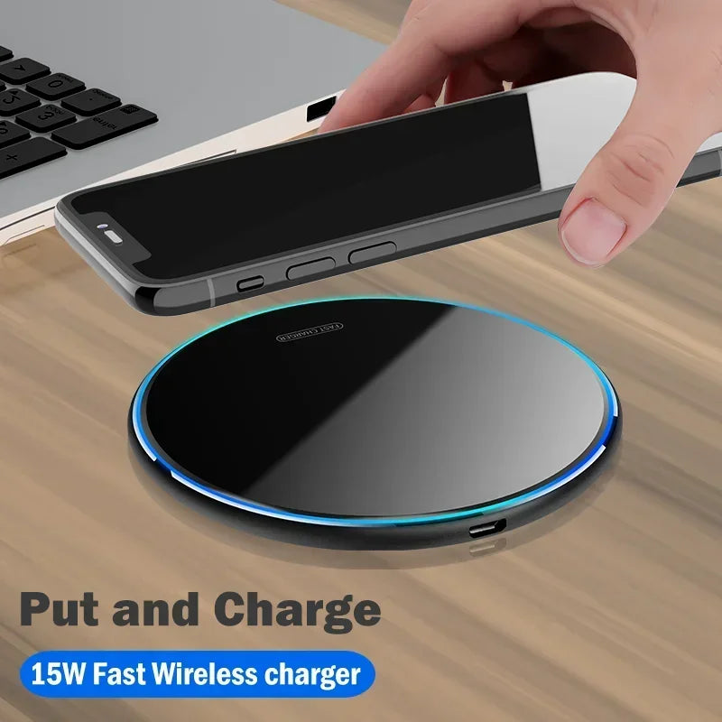 A hand holds a smartphone above a sleek 15W fast wireless charging pad on a wooden surface near a laptop keyboard. Text reads, "Put and Charge 15W Fast Wireless Charger."