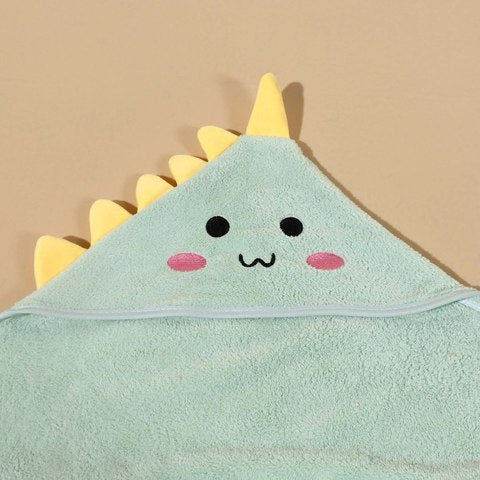 Cute dinosaur-themed green hooded towel with a smiling face, pink cheeks, and yellow fabric spikes on a plain background, ideal for kids' bath time or dress-up.