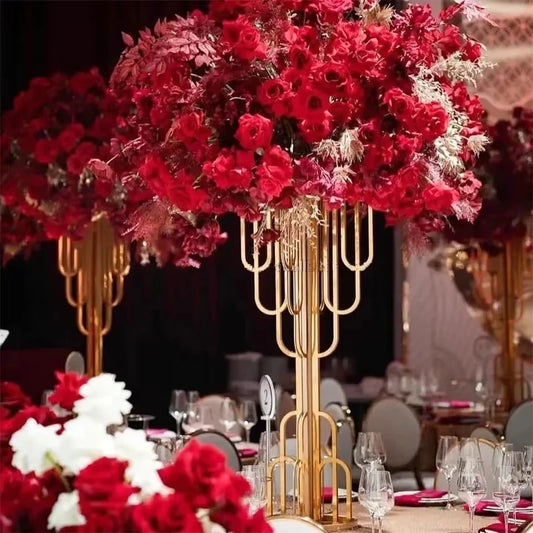 Elegant table setting with tall gold stands holding lush red floral arrangements, surrounded by white chairs and wine glasses, creating a luxurious atmosphere.