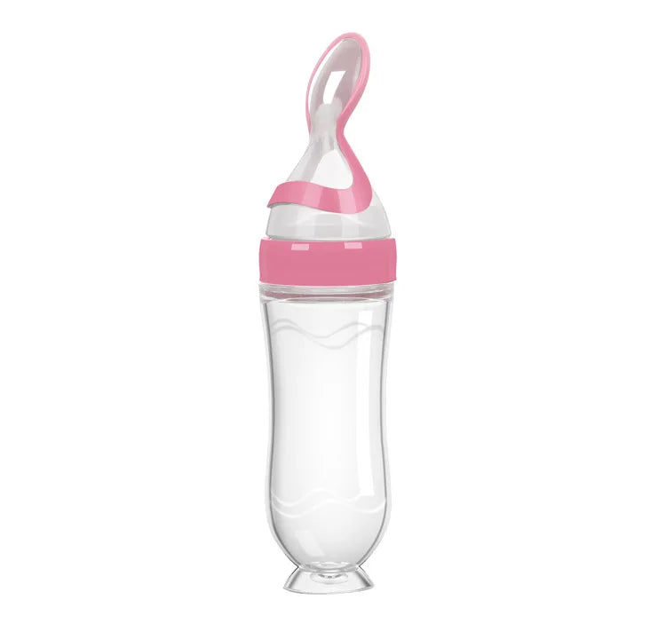 Clear baby bottle with a pink cap and spoon tip. The design is ergonomic with a wavy grip and a suction base. Ideal for easy feeding and minimal spills.