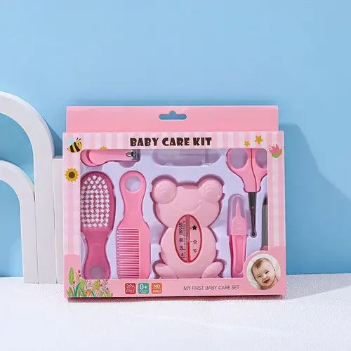 Pink baby care kit featuring a teddy bear-shaped thermometer, brush, comb, nail clipper, and dropper, packaged with playful decorations. Labeled "My First Baby Care Set".