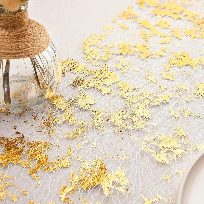 Glass vase wrapped with twine on a textured surface scattered with gold leaf flakes, creating an elegant, artistic arrangement.