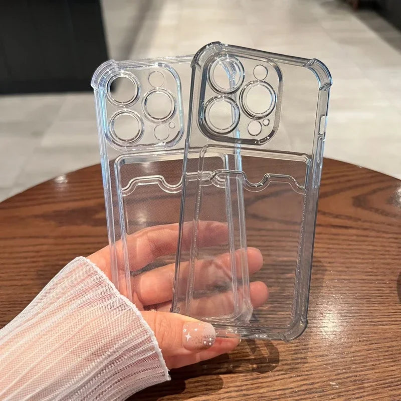 A hand holds two transparent phone cases with card slots on a wooden table. The cases have camera cutouts suitable for a smartphone with multiple lenses.