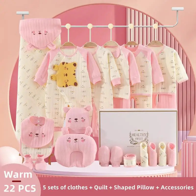 A set of pink and cream baby clothes and accessories, including outfits, a quilt, a hooded blanket, bib, socks, mittens, pillows, and rolled blankets on a pink background.
