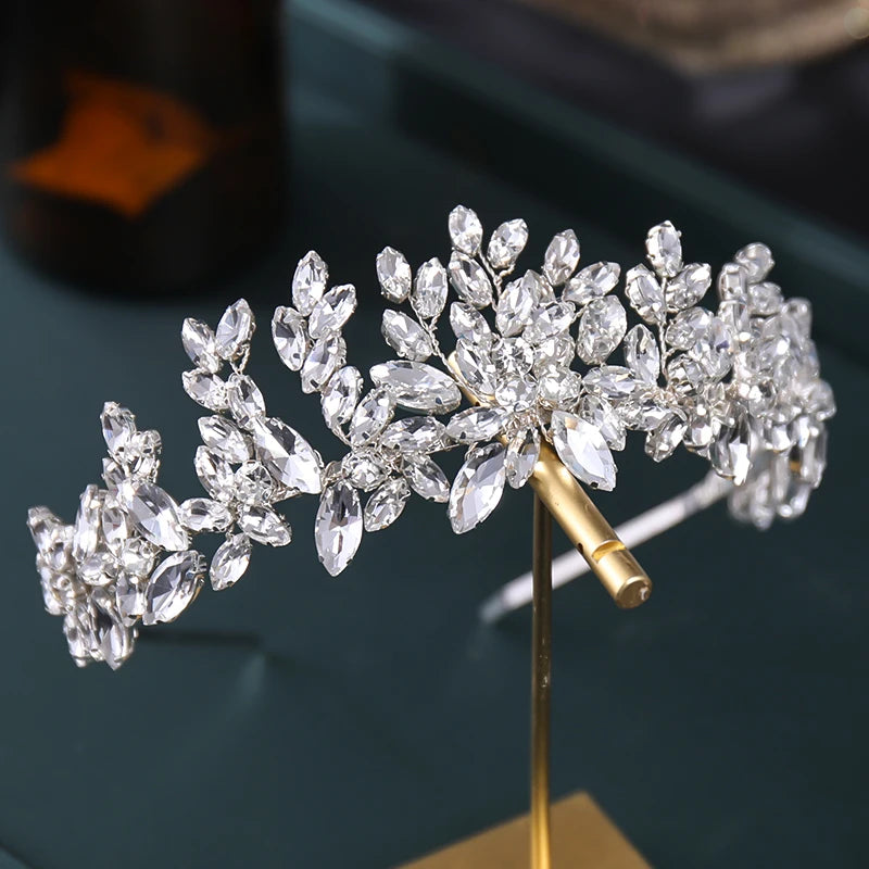 Elegant tiara with intricate crystal leaf design, displayed on a stand against a dark background.